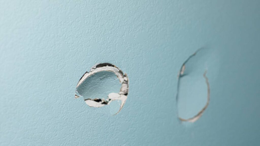 a blue wall with two holes in the sheetrock from a wall being punched by hand