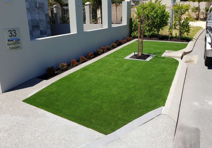 Green synthetic grass at the front yard of a house next to a gutter and road.