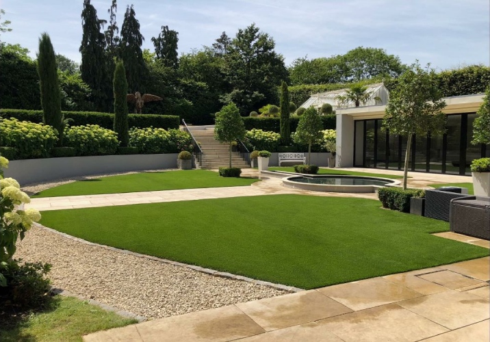 Large, well-manicured backyard with synthetic grass, water feature and hedges.