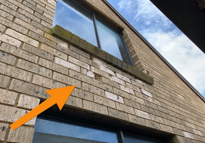 A two storey brown brick home with an orange arrow pointing to a damaged area